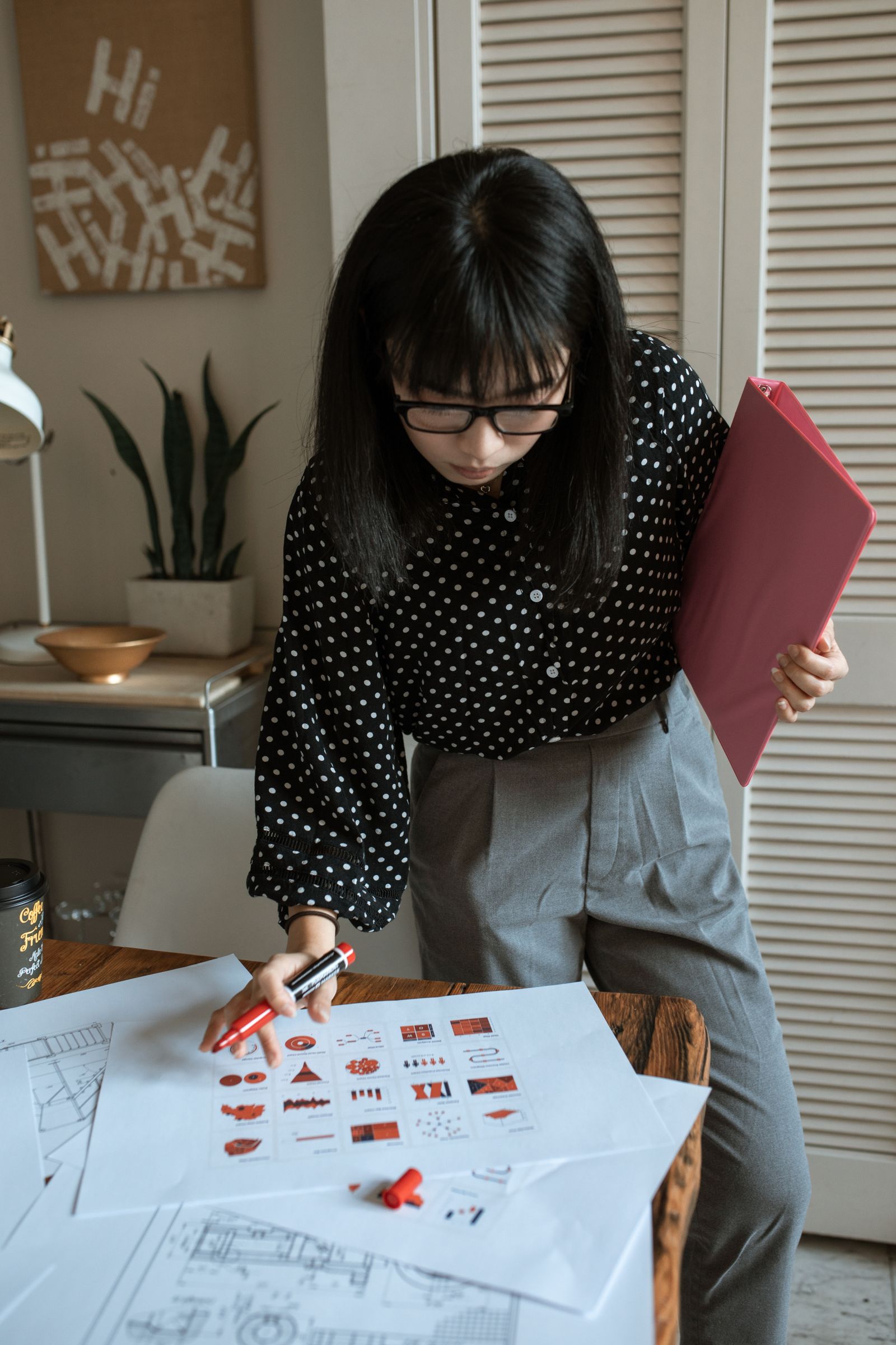 Một phụ nữ xem tài liệu thiết kế tại bàn làm việc trong phòng có cây xanh.
